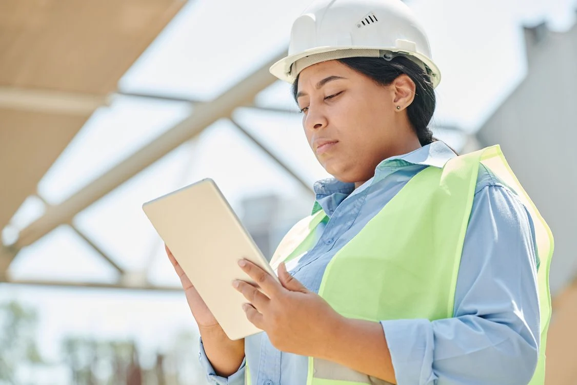 Engineer in a hard hat and high-visibility vest using a tablet on site